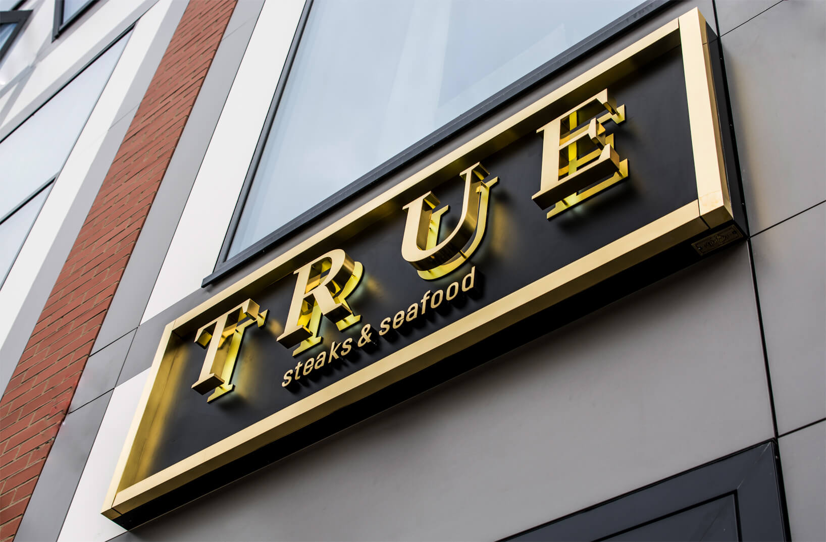 True - rótulo exterior con letras doradas en acero inoxidable